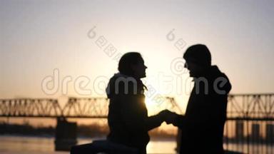 年轻的幸福夫妇牵着彼此`手，微笑着面对美丽的夕阳和铁路桥。 4k